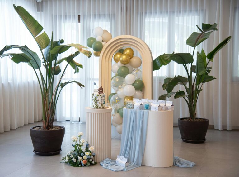 Beautiful indoor party decoration with balloons, plants, and curtain backdrop.
