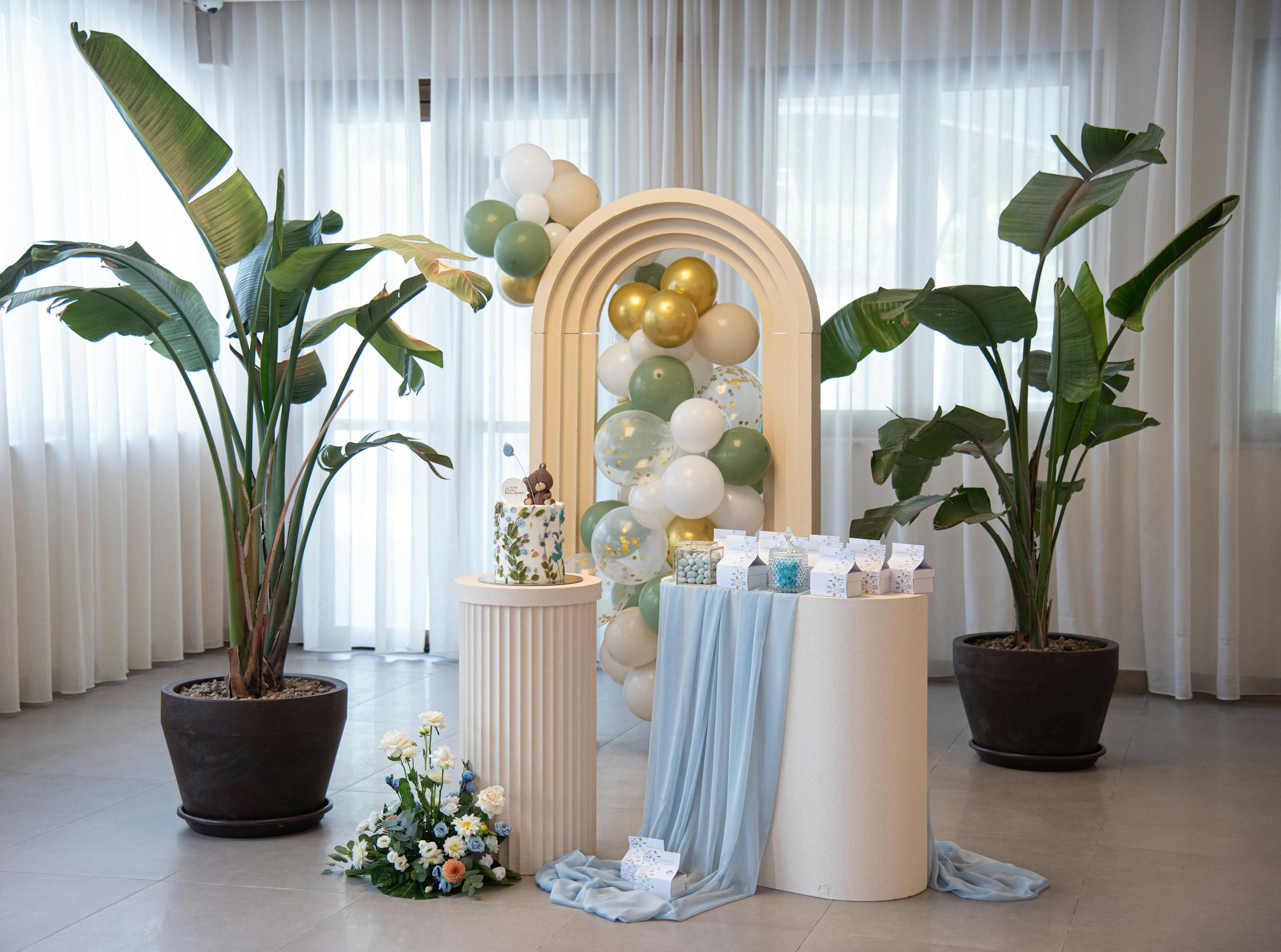 Beautiful indoor party decoration with balloons, plants, and curtain backdrop.
